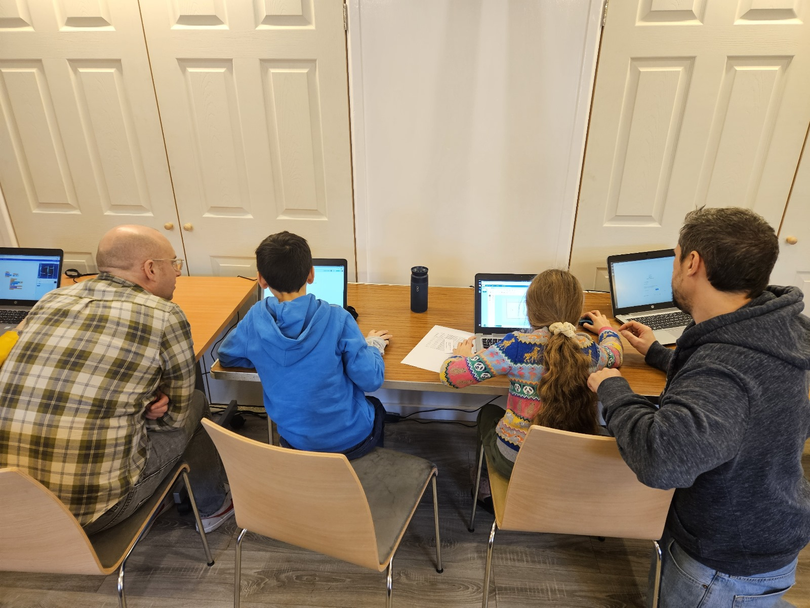 A picture of a brother and sister sat at laptops building their ghost chase game, they are being guided by myself and a fellow volunteer